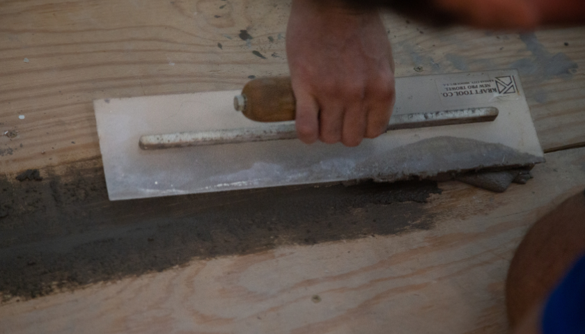 This image shows a notch trowel applying a grout to a wood floor.