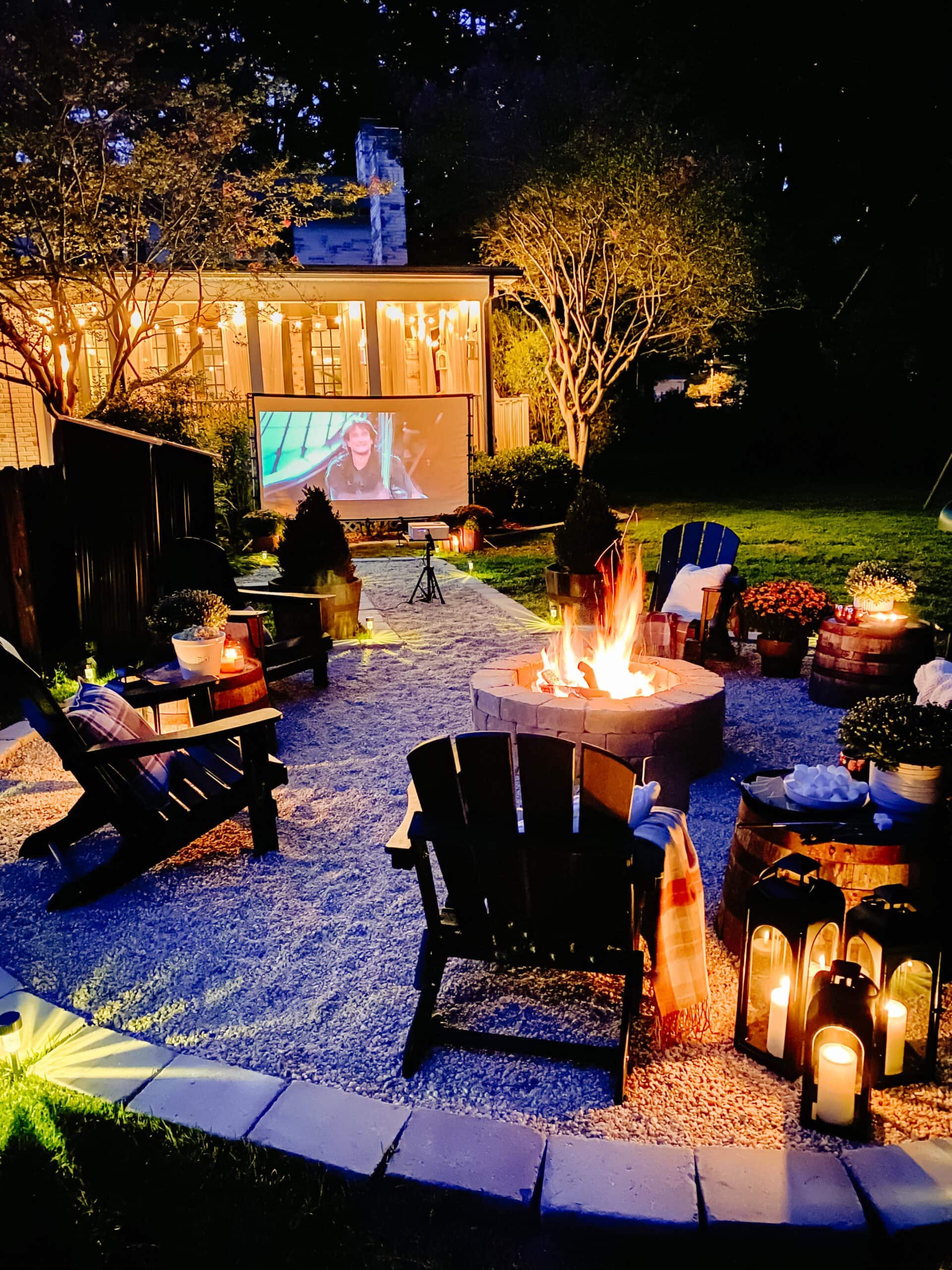 a backyard movie night setup around a fire pit with mums, blankets, and fall decor