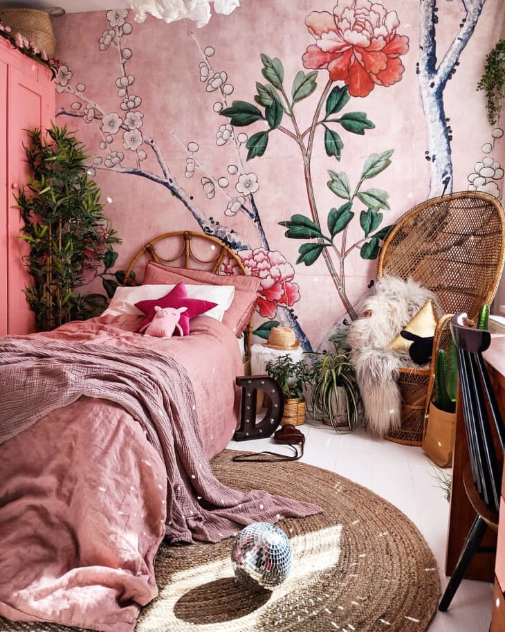 A bedroom with a pink bedspread, pink pillows, and pink floral wallpaper