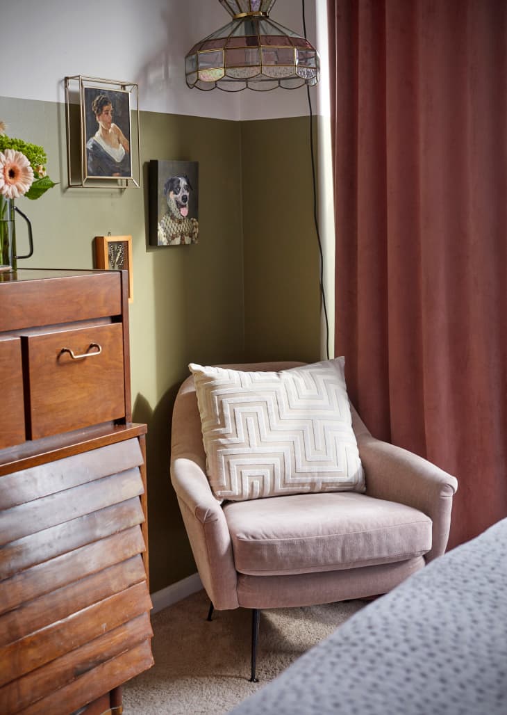 Corner of bedroom with pale pink armchair. foot of bed and part of vintage dresser visible. Walls painted halfway with olive green