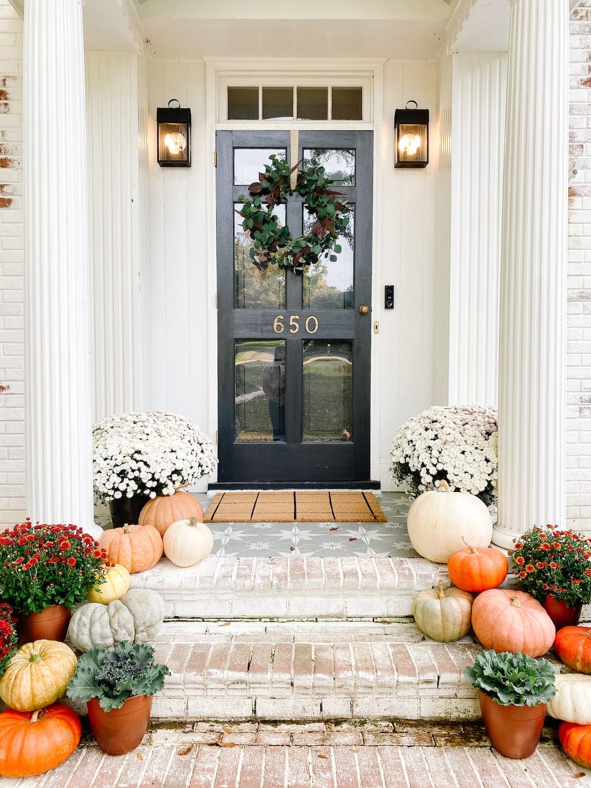 fall wreath on a front door and porch decorated with pumpkins and mums